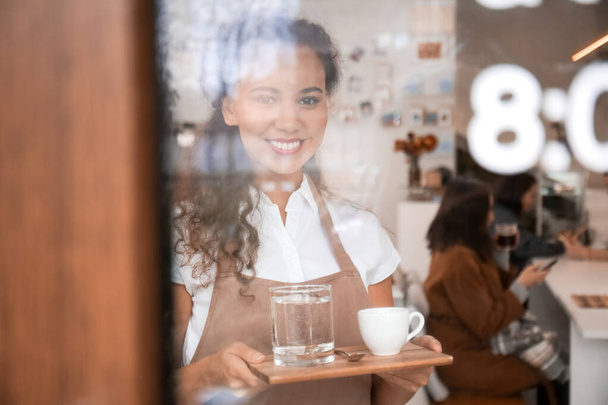 Fiatal barista egy csésze forró eszpresszó kávézó, kilátás üvegajtón keresztül - Fotó, kép