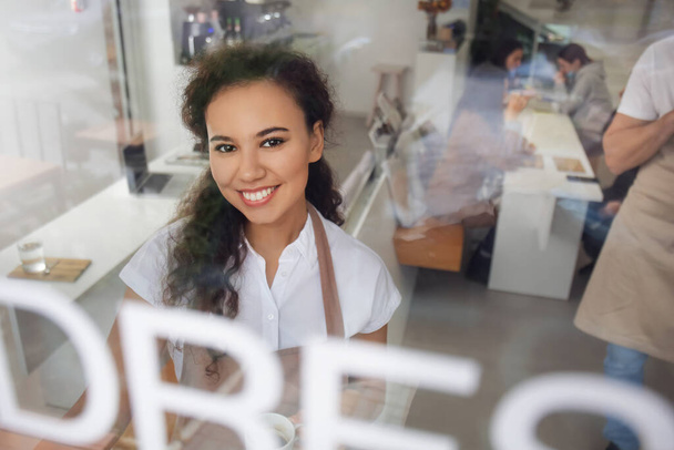 Jeune barista dans un café, vue à travers une porte vitrée - Photo, image