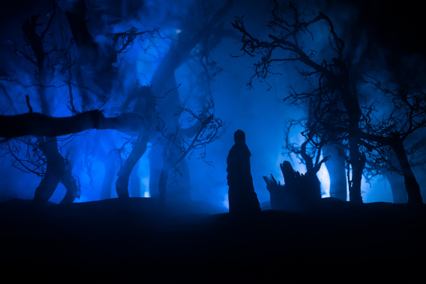 Μόνη στο νεκρό δάσος τη νύχτα με ομίχλη. Η σιλουέτα του κοριτσιού που στέκεται ανάμεσα στα δέντρα κάτω από το φως του φεγγαριού. Φρίκη Απόκριες έννοια. Επιλεκτική εστίαση. - Φωτογραφία, εικόνα