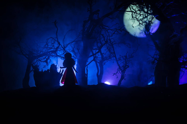 Alone girl in the dead forest at misty night. Silhouette of girl standing between trees under moonlight. Horror Halloween concept. Selective focus. - Photo, Image