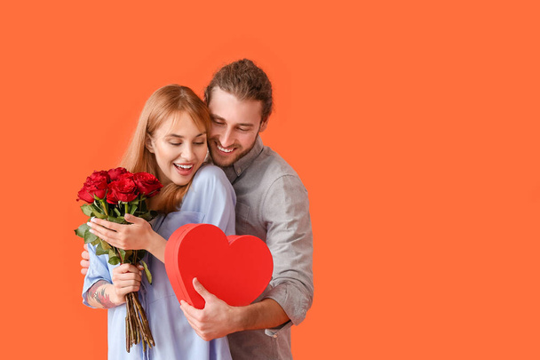 Молодая пара с цветами и подарком на цветном фоне. Празднование Дня Святого Валентина - Фото, изображение