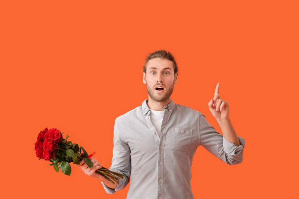 花を持つ若い男と背景色に人差し指を上げました。バレンタインデーのお祝い - 写真・画像