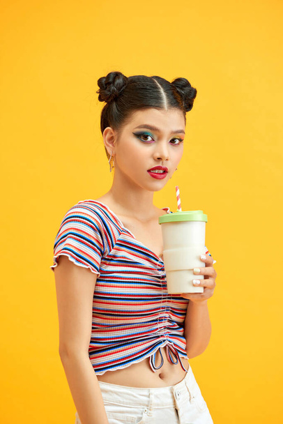 黄色の背景に隔離された縞模様のTシャツ飲料チョコレートを身に着けている魅力的な女の子の肖像画 - 写真・画像