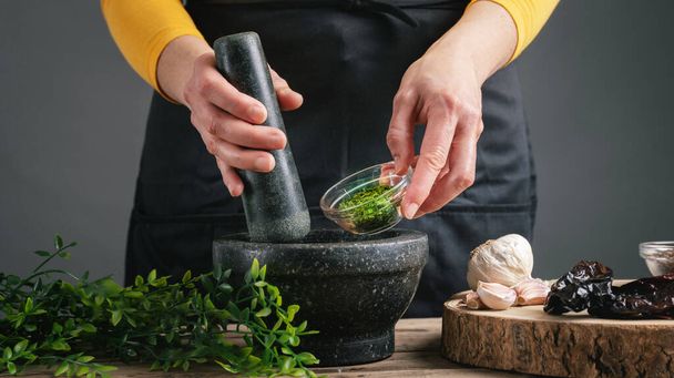 Female cook's hands pouring chopped parsley into the mortar - Фото, зображення