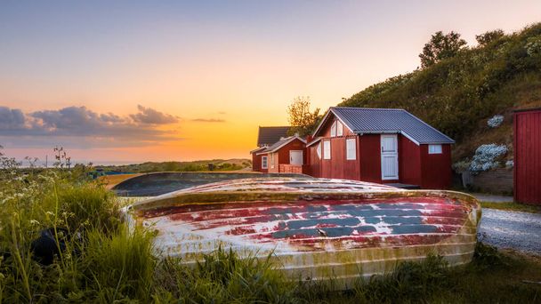 a mesmerizing shot of red wooden houses and colorful boats on the sunset background - 写真・画像