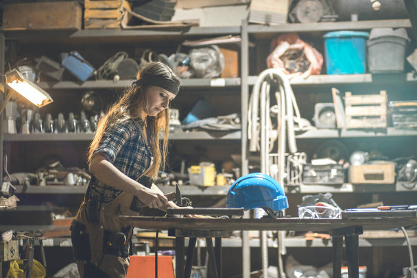 mujer joven que trabaja en la mesa usando un martillo en un taller - Foto, imagen