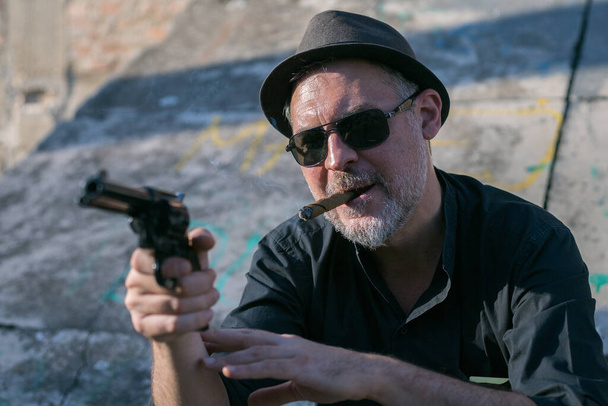 mafioso middle age man smoking cigar outdoors and holding a gun replica - Valokuva, kuva