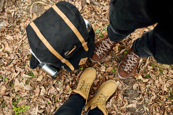Moderní mladý pár v turistických botách stojící v lese s cestovní taškou, venkovní cestovní koncept, pohled shora, Láska navždy, Valentýn. - Fotografie, Obrázek