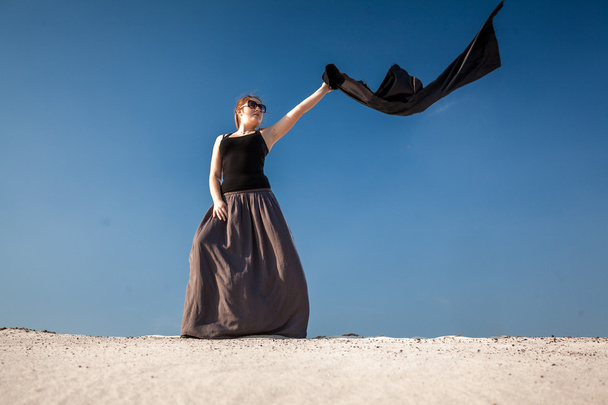 woman in long dress with black cloth standing on sand dune - 写真・画像