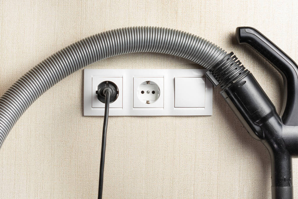 the vacuum cleaner cord is plugged into an electrical outlet on the wall. next to the hose from the vacuum cleaner. copy space. - Photo, Image