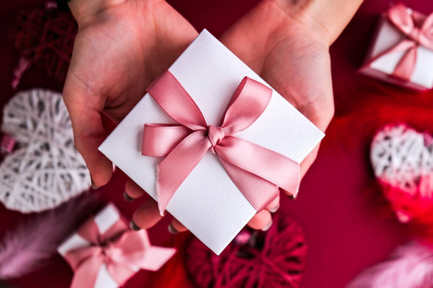 Pose plate de mains de femme tenant présent avec boîte décorée de ruban rose sur fond rouge. Joyeuse Saint Valentin. Noël, la fête des mères. Carte de voeux - Photo, image