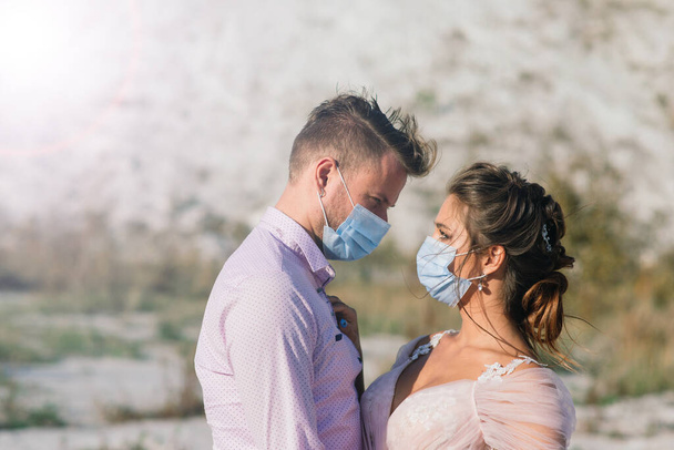Mladý milující pár procházející se v lékařských maskách v parku během karantény v jejich svatební den. - Fotografie, Obrázek