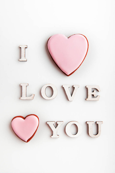 I LOVE YOU nápis na bílém pozadí vedle perníkové sušenky s růžovou polevou - Fotografie, Obrázek