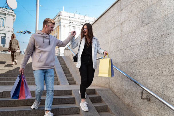 Glückliches junges Paar spaziert mit bunten Einkaufstüten durch die Stadt. - Foto, Bild
