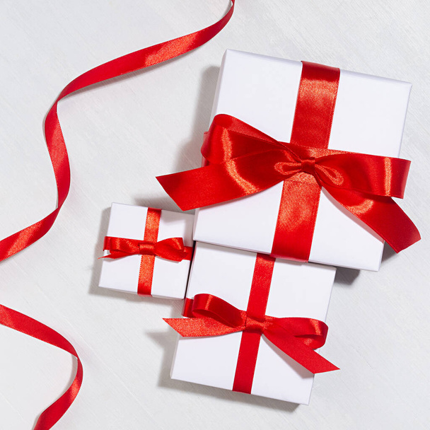White gift different size boxes with red silk bow, ribbon on white wood table, top view, square, valentine's day background. - Foto, imagen
