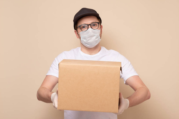 Livraison homme tenant boîte en carton dans des gants en caoutchouc médical et masque - Photo, image