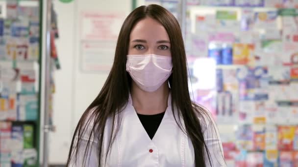 Una mujer con una máscara médica, bata y guantes, muestra un frasco de medicamentos. En el fondo, cajas de vidrio con medicamentos. Concepto de pandemia viral y protección contra la infección. - Metraje, vídeo