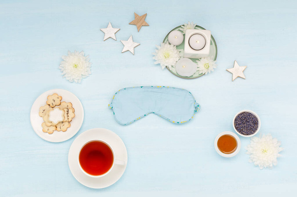Cotton sleep mask, homemade cookies, cup of herbal tea, dry lavender flowers and candles on blue background. Top view, copy space. Healthy night sleep creative concept in blue colors.  - Photo, Image