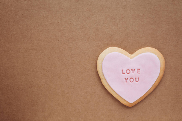 Печиво у формі серця з рожевою глазур'ю та написом: любов, яку ви розміщуєте на паперовому тлі ремесла з пробілом для вашого тексту
 - Фото, зображення