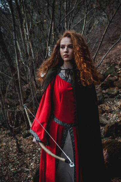 Red-haired woman in a red dress in a historical Celtic costume in the autumn forest - Photo, image