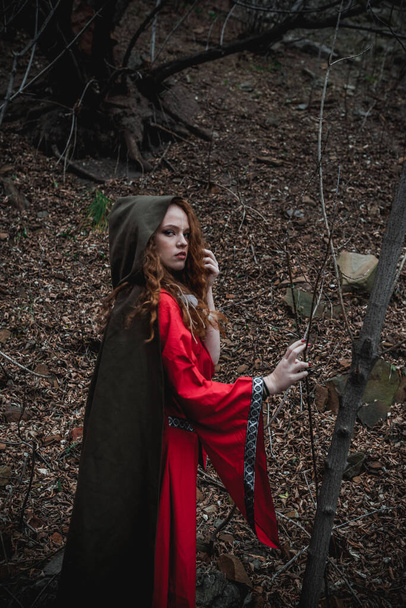 Red-haired woman in a red dress in a historical Celtic costume in the autumn forest - Valokuva, kuva