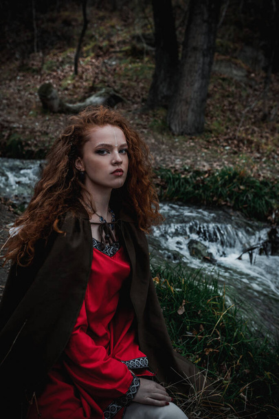 Red-haired woman in a red dress in a historical Celtic costume in the autumn forest - Fotó, kép