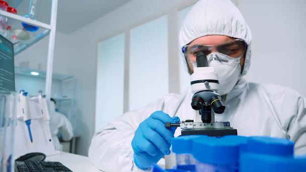 Scientist in ppe suit conducting experiment using microscope - Foto, Bild