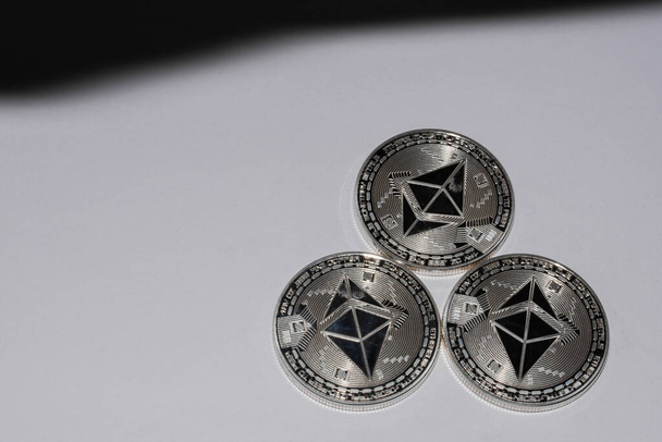 три срібні ефірні монети з криптовалюти на білому і маленькому чорному тлі з тіні
 - Фото, зображення