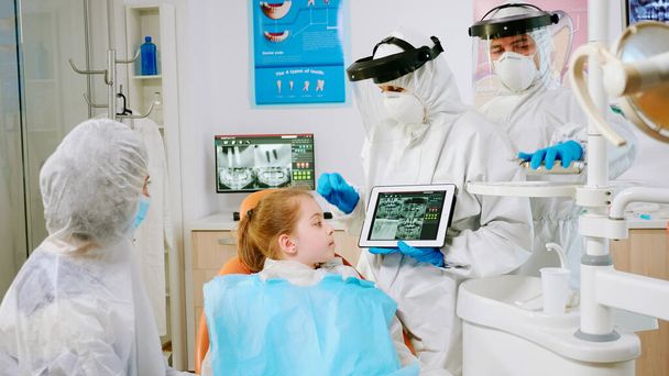 Dentysta w sprzęcie ochronnym pokazujący na tablecie prześwietlenie stomatologiczne - Zdjęcie, obraz