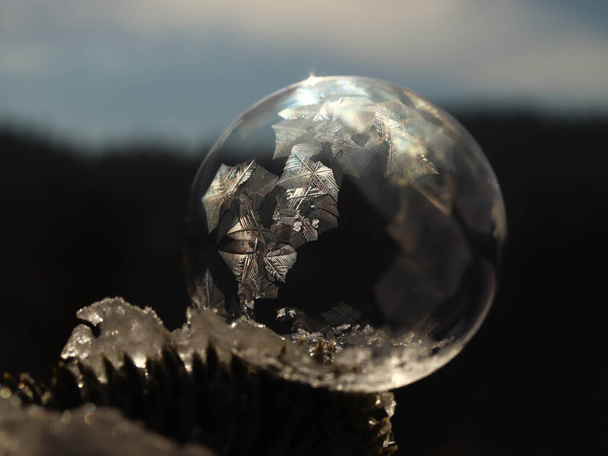ice bubble with a frozen ornament on the surface against the sun with the sun in the background - 写真・画像