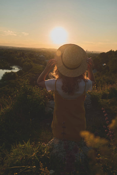 menina em um chapéu de palha em um fundo por do sol - Foto, Imagem