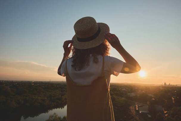 meisje in een stro hoed op een zonsondergang achtergrond - Foto, afbeelding