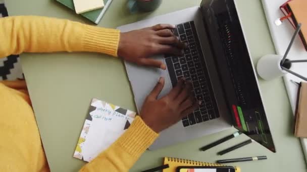 Проміжок часу зверху вниз знімок рук невпізнаваного чорного чоловіка, який працює на ноутбуці, використовуючи смартфон і роблячи нотатки на офісному столі
 - Кадри, відео