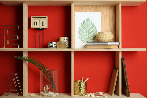 Stylish wooden shelves with decorative elements on red wall - Foto, imagen