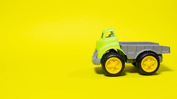Speelgoedauto op een gele achtergrond - bouwmateriaal voor kinderen. Lichte kinderen plastic speelgoed, dump truck kindertijd - Foto, afbeelding