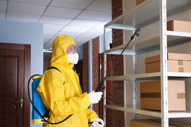 Pest control worker spraying pesticide on rack indoors - Фото, зображення