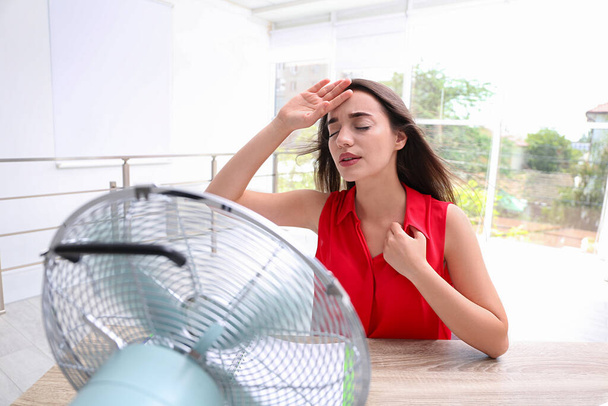 Woman with fan suffering from heat at workplace. Summer season - 写真・画像