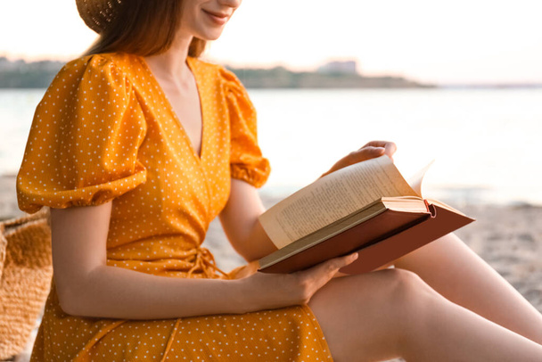 Young woman reading book on sandy beach near sea, closeup - Foto, Imagem