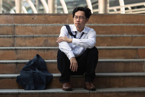 Deprimido estresado joven asiático hombre de negocios en traje con las manos en la cabeza sentado en las escaleras. Concepto de desempleo y despido. - Foto, Imagen