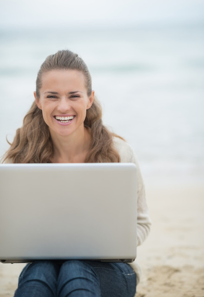 Woman sitting with laptop on beach - 写真・画像