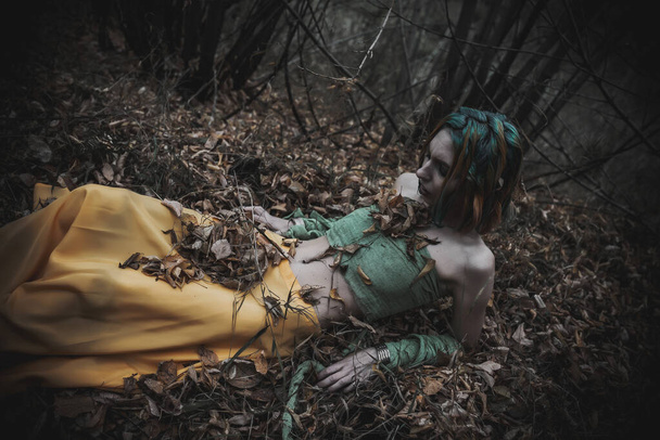 dead girl in autumn foliage wearing green and yellow robes - Valokuva, kuva