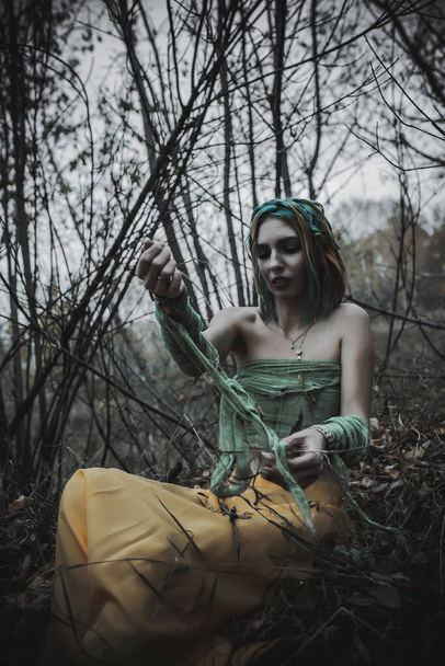 dead girl in autumn foliage wearing green and yellow robes - Фото, изображение