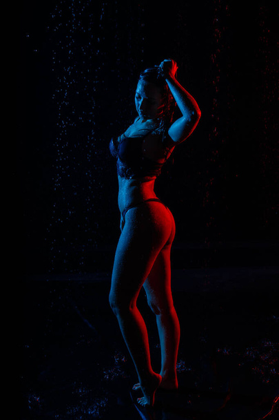 Female in the white shirt with water drop in a dark room illuminated by light during a photoshoot with water in a small pool - Fotoğraf, Görsel