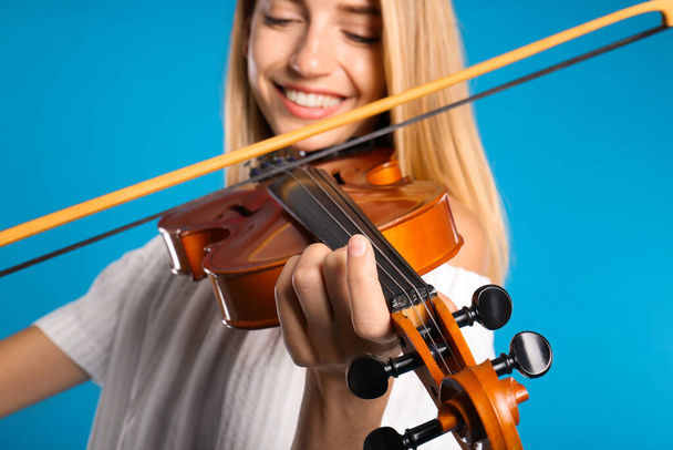 Beautiful woman playing violin on light blue background, closeup - Фото, изображение