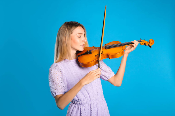 Beautiful woman playing violin on blue background - Фото, зображення
