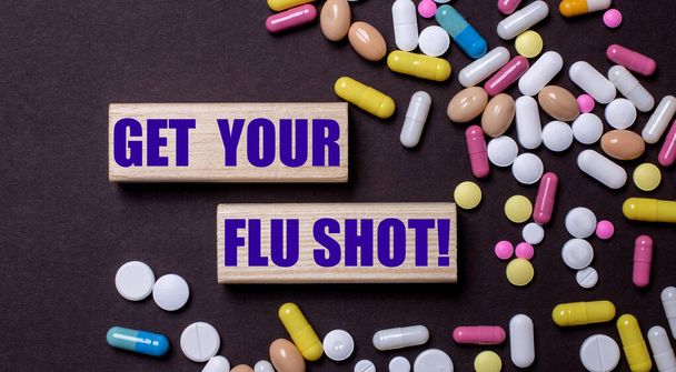 GET YOUR FLU SHOT is written on wooden blocks near multi-colored pills. Medical concept - Photo, image