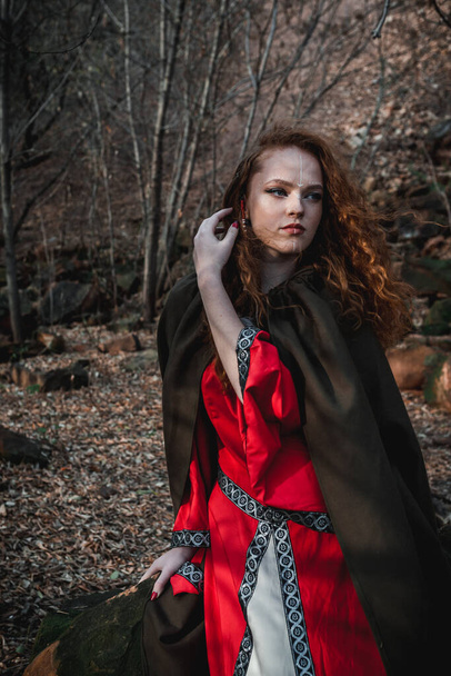 Red-haired woman in a red dress in a historical Celtic costume in the autumn forest - Foto, Imagem