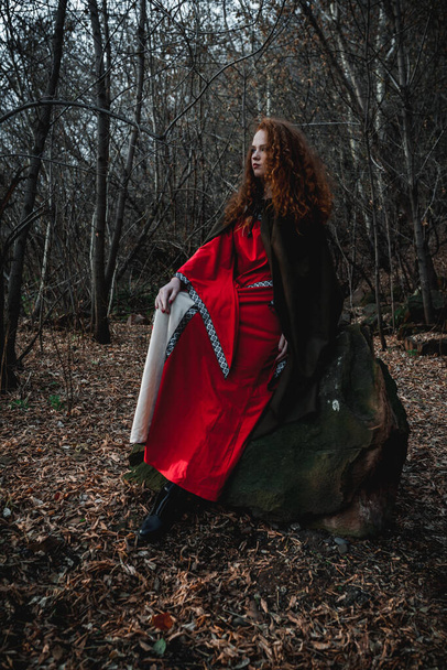 Mulher de cabelos vermelhos em um vestido vermelho em um traje celta histórico na floresta de outono - Foto, Imagem
