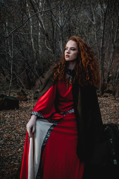 Red-haired woman in a red dress in a historical Celtic costume in the autumn forest - Foto, Bild