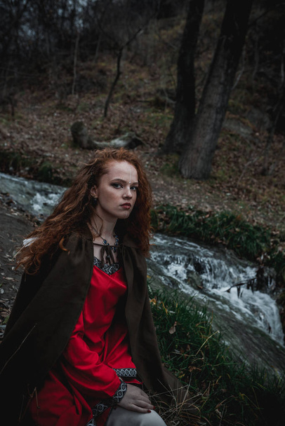 Red-haired woman in a red dress in a historical Celtic costume in the autumn forest - Fotografie, Obrázek